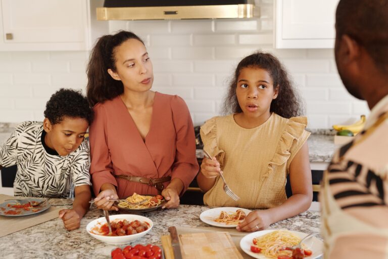 Family gathered around the kitchen table enjoying a pasta dinner together at home.