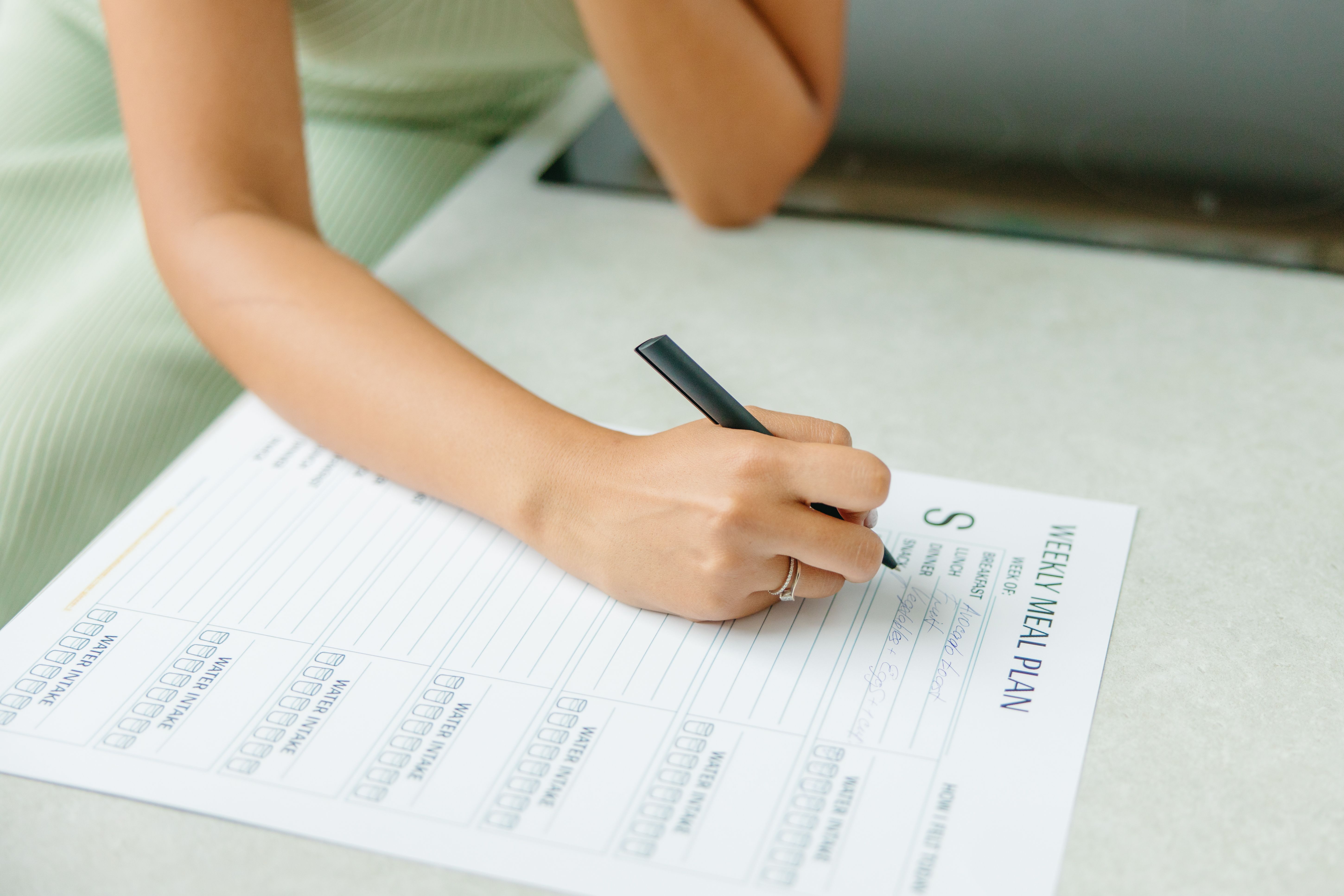 Woman writing a weekly meal plan at home with a notebook and food nearby.